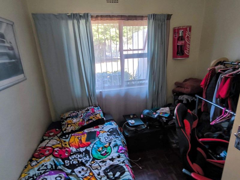 A compact bedroom featuring parquet flooring and a window fitted with security bars, providing natural light and essential security.