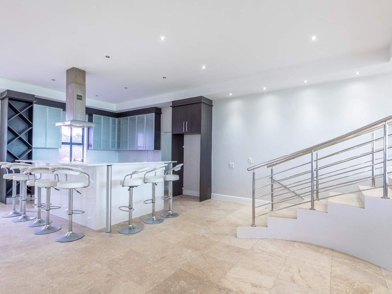 Modern open-plan kitchen featuring a central island, sleek cabinetry, and an adjacent staircase with a contemporary stainless steel balustrade.
