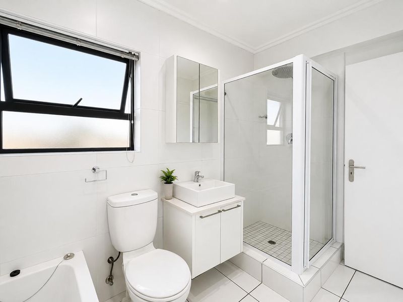 A modern, well-maintained bathroom featuring a glass shower enclosure, a contemporary vessel sink vanity, and clean white wall tiling.