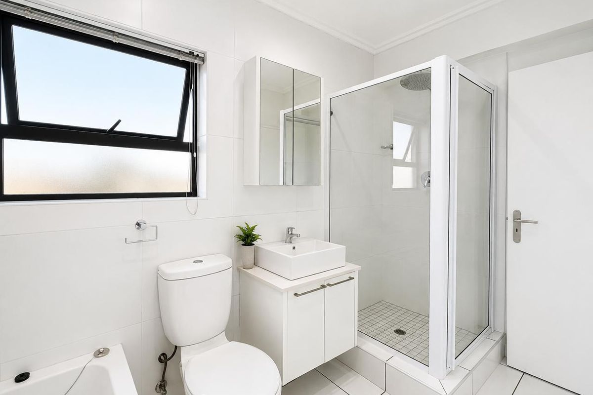 A modern, well-maintained bathroom featuring a glass shower enclosure, a contemporary vessel sink vanity, and clean white wall tiling.