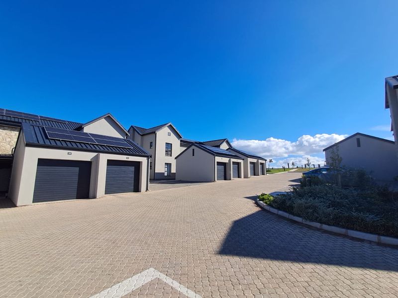 A modern apartment complex exterior featuring paved driveway access, multiple garage units, and roof-mounted solar panels under a clear blue sky.