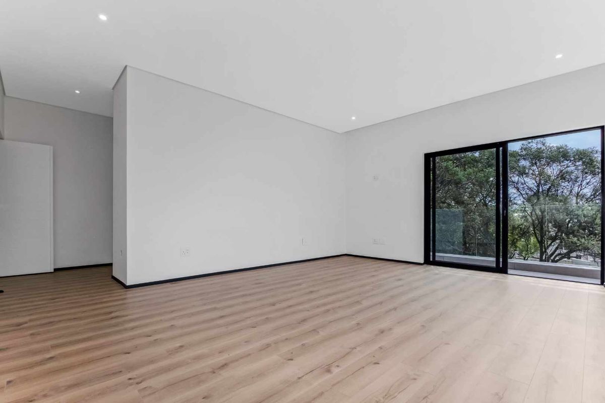 A bright and spacious living area featuring modern wood-look flooring, recessed ceiling lighting, and large sliding glass doors opening to an outdoor balcony.