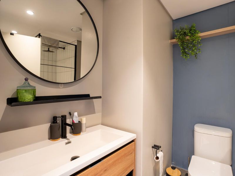 Modern bathroom featuring a sleek vanity with integrated sink, round mirror, contemporary black fixtures, and a glass-enclosed shower with tiled walls.
