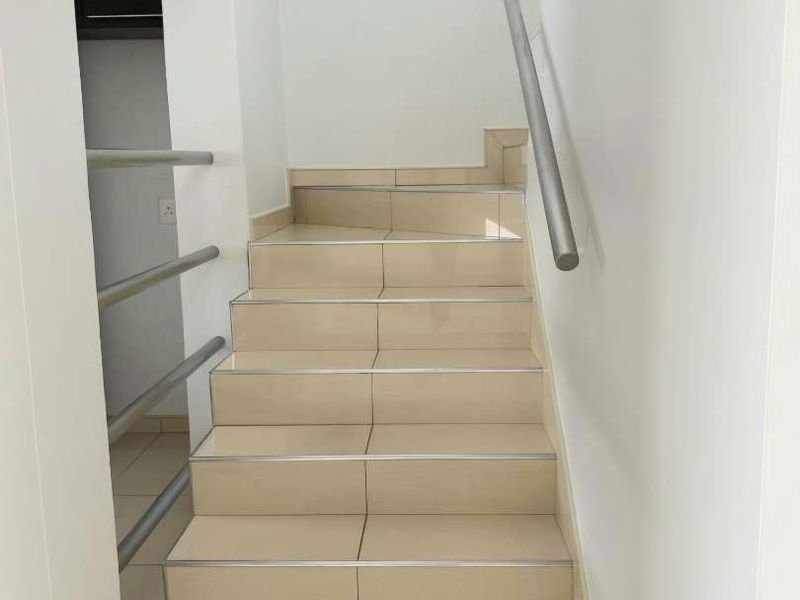 A clean, modern staircase featuring neutral floor tiles, a sleek metal handrail, and integrated built-in shelving in the adjacent wall niche.
