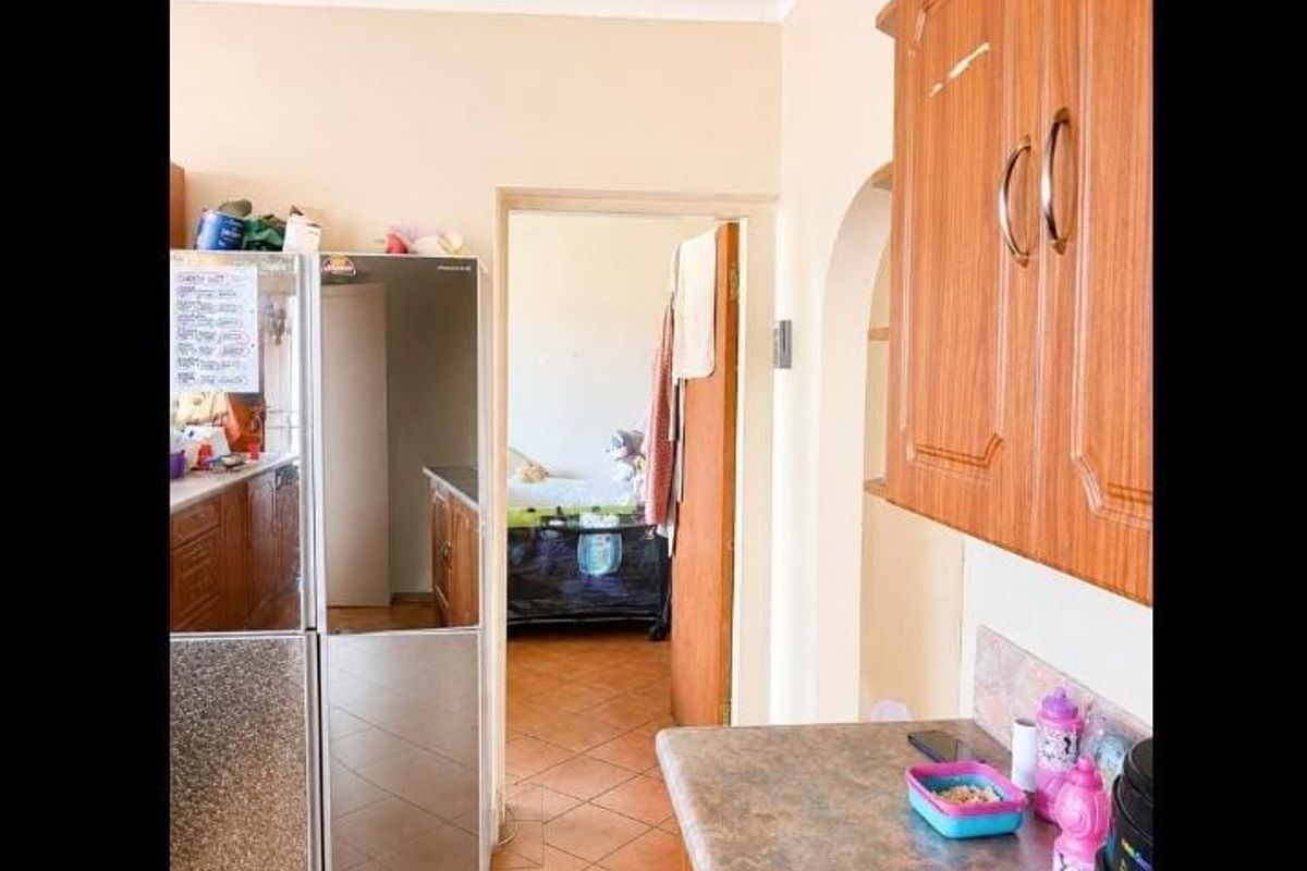 A kitchen area featuring wood-look laminate cabinetry, durable laminate countertops, and tiled flooring, with an open archway leading to an adjacent room.