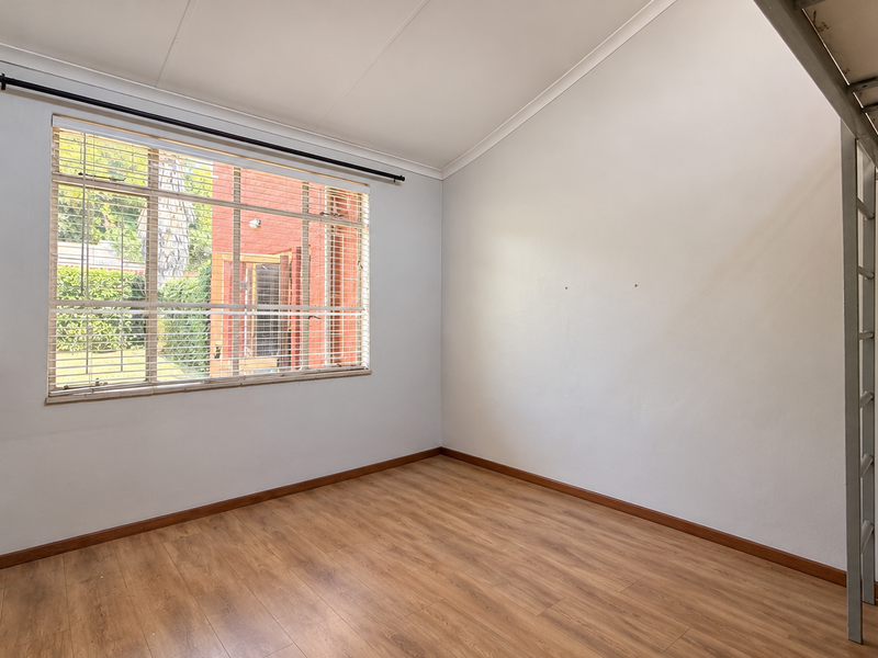 A bright, empty bedroom featuring laminate flooring, built-in shelving, and a fixed loft bed frame with a ladder.