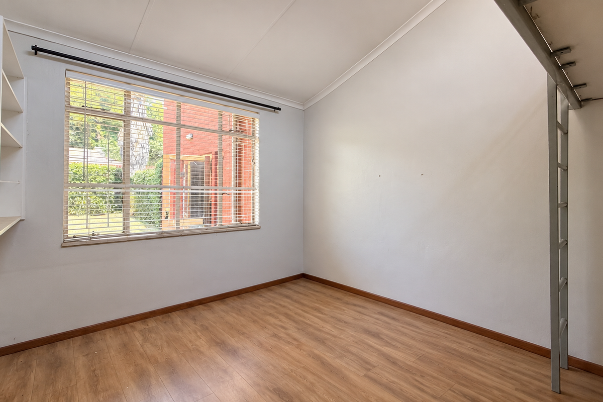 A bright, empty bedroom featuring laminate flooring, built-in shelving, and a fixed loft bed frame with a ladder.