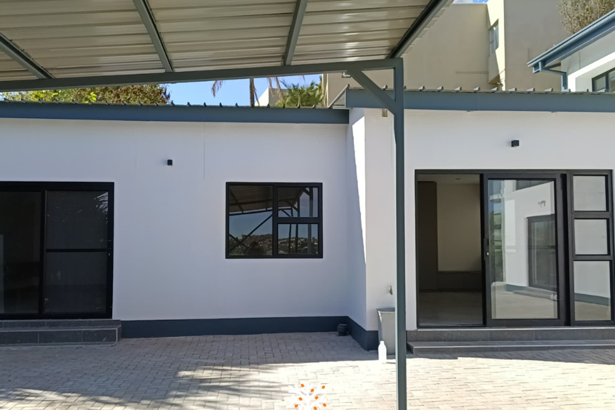 A well-maintained exterior rear view featuring a paved courtyard, covered patio area, and modern sliding glass doors with dark frames.