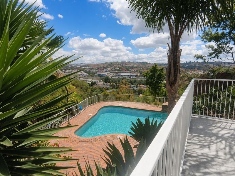 Outdoor pool area featuring a brick surround, metal safety railing, and elevated views of the surrounding landscape.