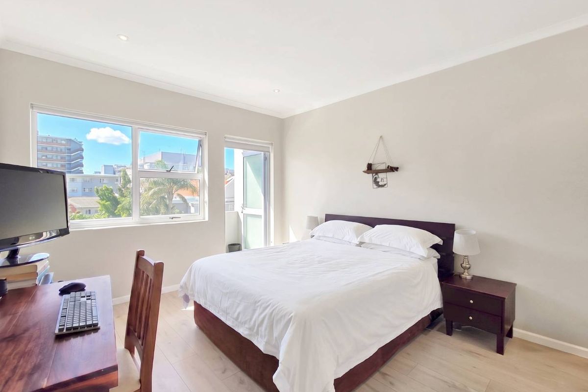 A bright and well-maintained bedroom featuring light laminate flooring, recessed downlighting, and direct access to a private balcony through a sliding glass door.