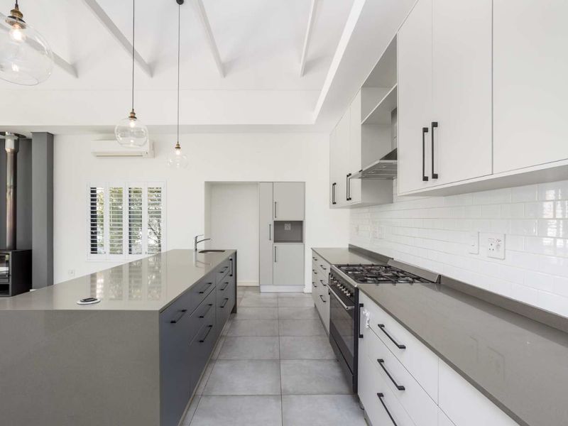 Modern kitchen featuring a large island, quartz countertops, gas cooktop, subway tile backsplash, and an adjacent wood-burning fireplace under an exposed beam ceiling.
