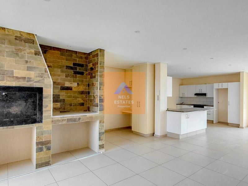 Spacious open-plan living area featuring a built-in stone-clad fireplace and a modern kitchen with ample cabinetry and a central island.