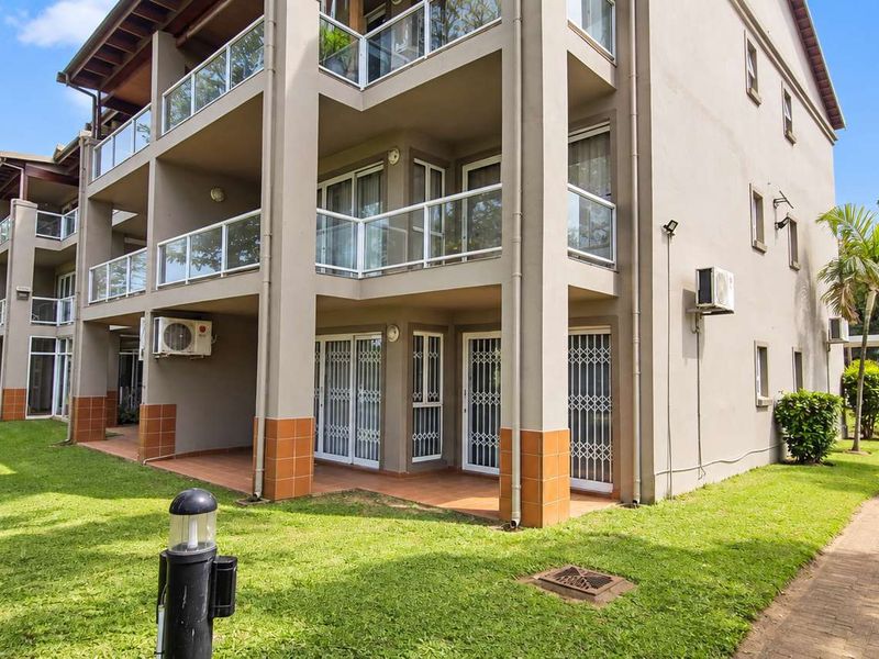 Rear elevation of a multi-story townhouse complex featuring private balconies with glass balustrades, ground floor patios, and well-maintained communal garden areas.