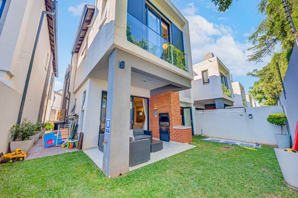 Rear view of a modern cluster home featuring a covered patio with a built-in braai, a private garden, and an upper-level balcony.