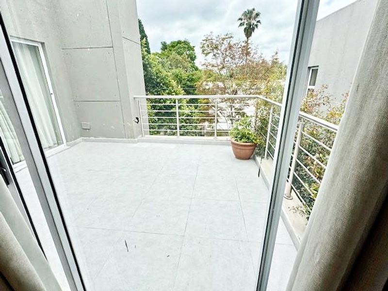 A spacious balcony featuring tiled flooring and a modern stainless steel balustrade, offering an open outdoor area accessible via sliding glass doors.
