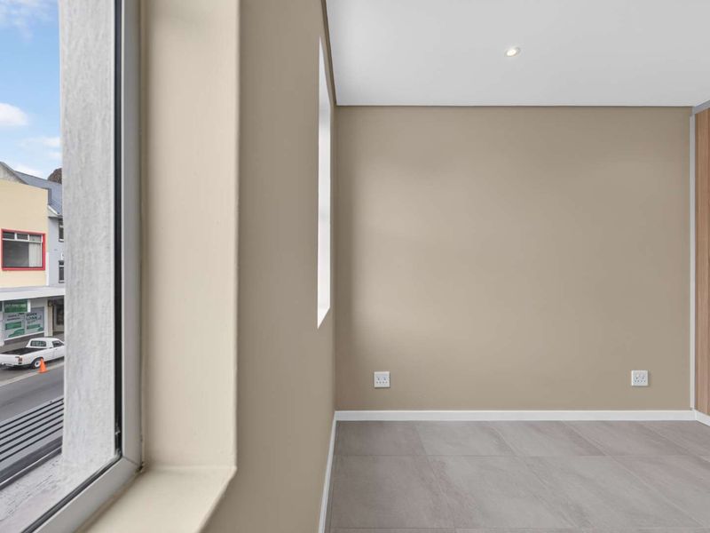 A bright, empty bedroom featuring modern tiled flooring, recessed downlighting, and a built-in wardrobe with wood-grain finish.