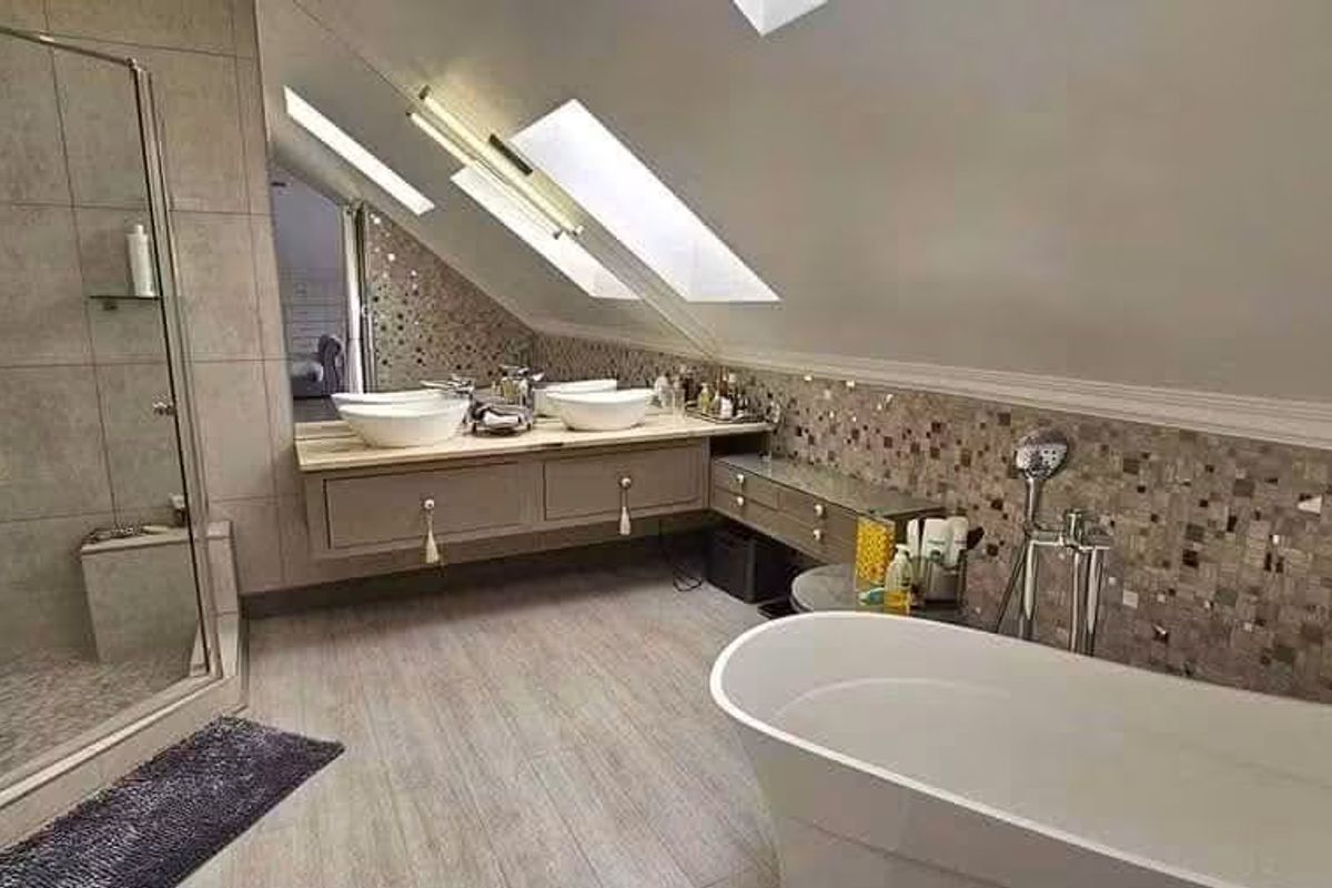 Modern attic bathroom featuring a freestanding bathtub, glass-enclosed shower, dual vessel sinks on a wall-mounted vanity, and natural light from skylights.