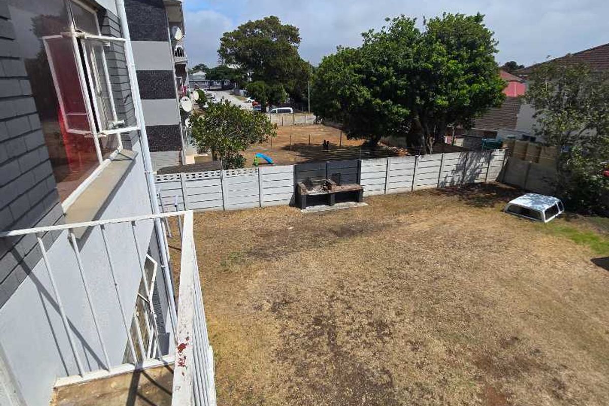 Elevated view of a private backyard featuring a built-in brick braai area, perimeter walling, and a balcony overlooking the garden space.