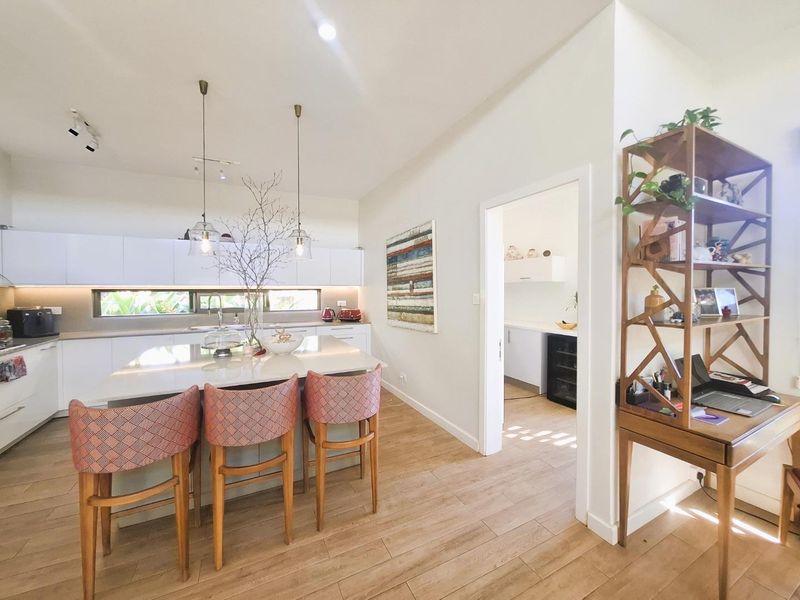 Modern open-plan kitchen featuring a central island with stone countertops, sleek cabinetry, and integrated lighting, with an adjacent scullery area.