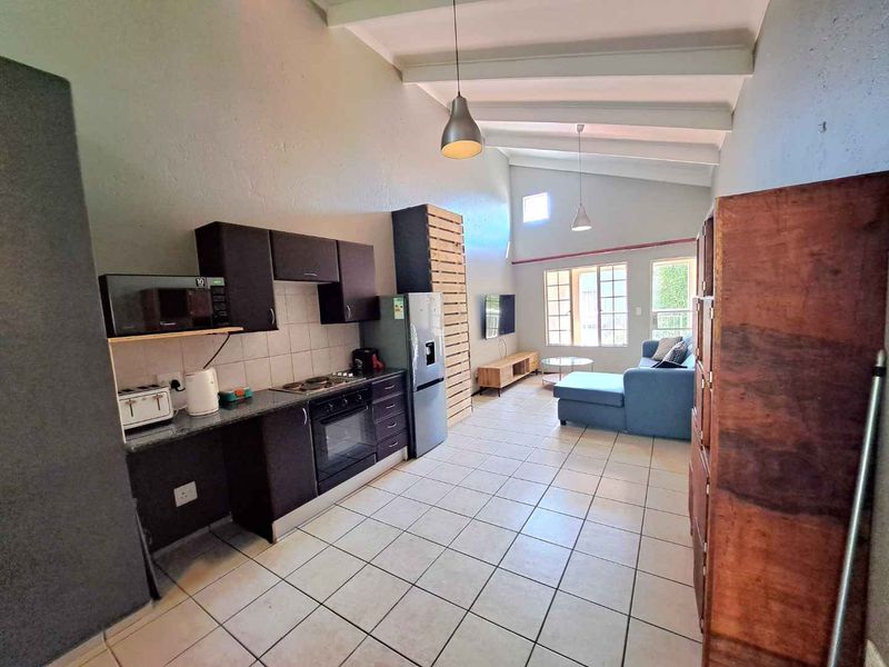Open-plan living area featuring a functional kitchen with built-in cabinetry, granite countertops, and high ceilings with exposed beams.