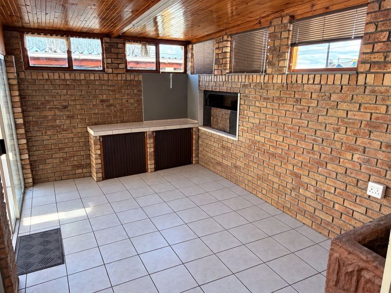 Covered patio area featuring exposed brick walls, tiled flooring, a timber ceiling, and a built-in braai, offering a functional outdoor entertainment space.