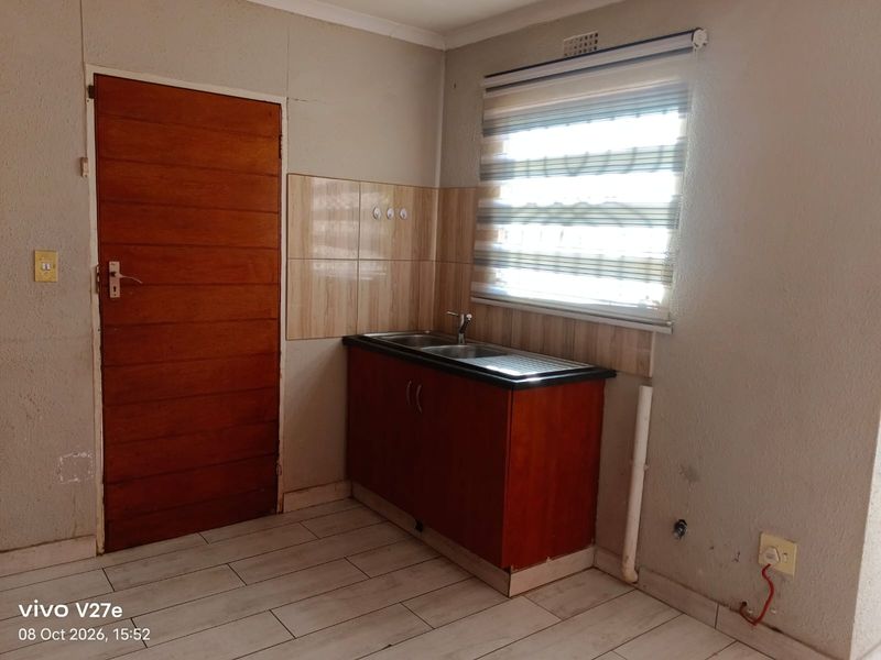 A compact kitchen area featuring a single sink unit, tiled splashback, and tiled flooring, requiring some maintenance to address exposed wiring and wall cracks.