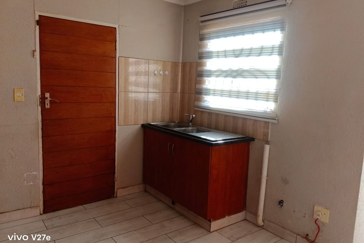 A compact kitchen area featuring a single sink unit, tiled splashback, and tiled flooring, requiring some maintenance to address exposed wiring and wall cracks.
