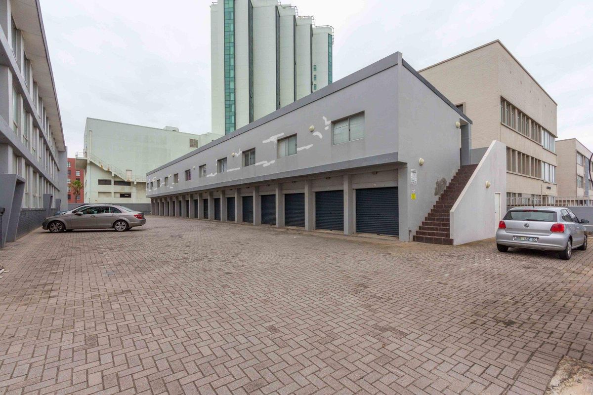 Exterior view of a multi-unit apartment complex featuring a paved parking area, row of roller shutter garages, and an external staircase.