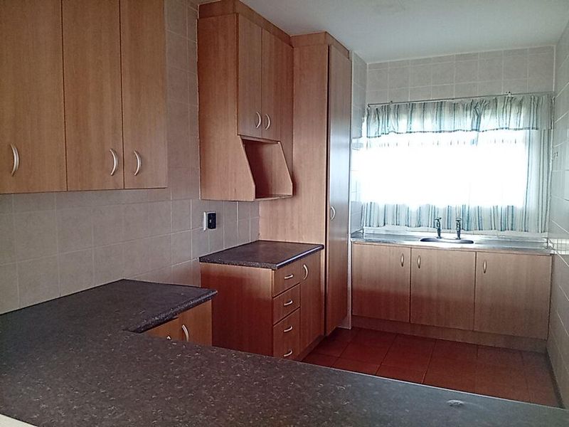 A functional kitchen featuring laminate cabinetry, dark countertops, tiled backsplash, and a stainless steel sink, offering a clean and practical layout.