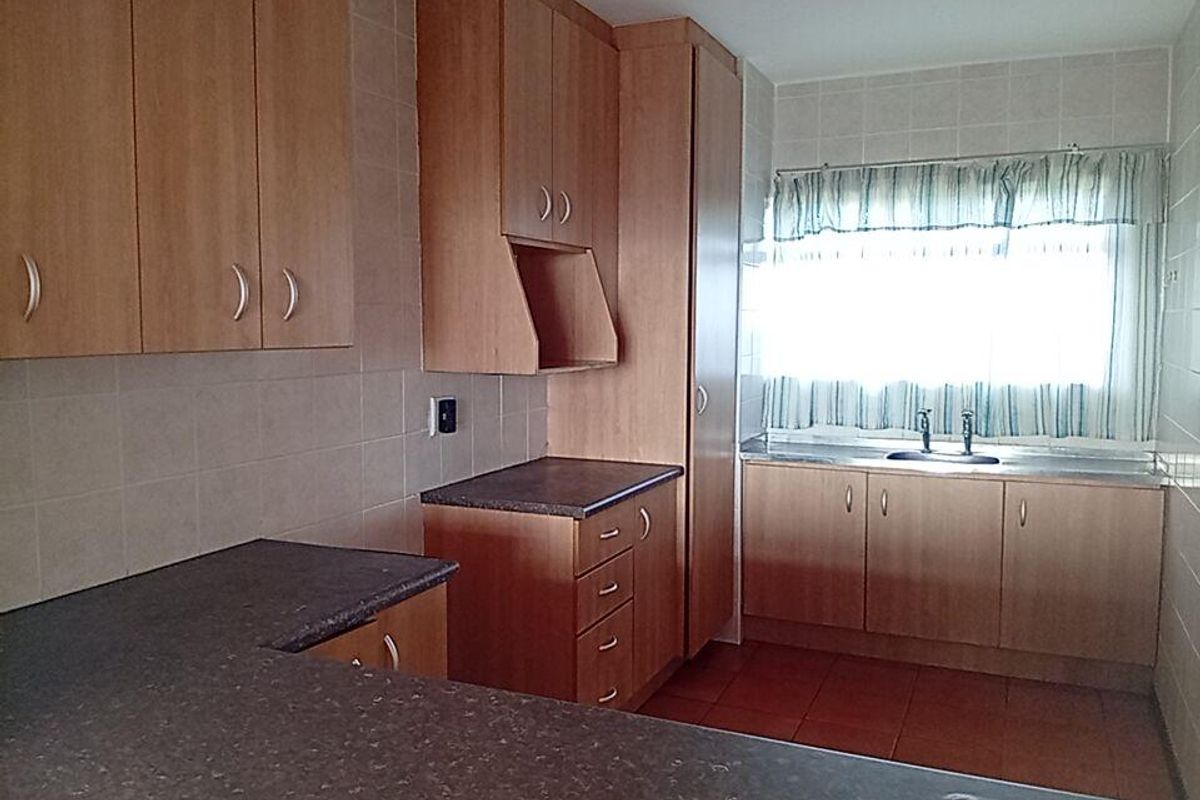 A functional kitchen featuring laminate cabinetry, dark countertops, tiled backsplash, and a stainless steel sink, offering a clean and practical layout.