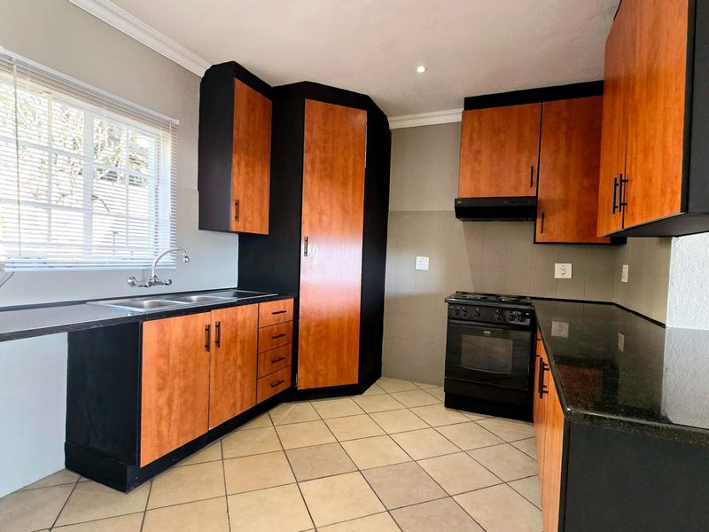 A functional kitchen featuring two-tone cabinetry, granite countertops, a double basin sink, and a freestanding stove with an extractor fan.
