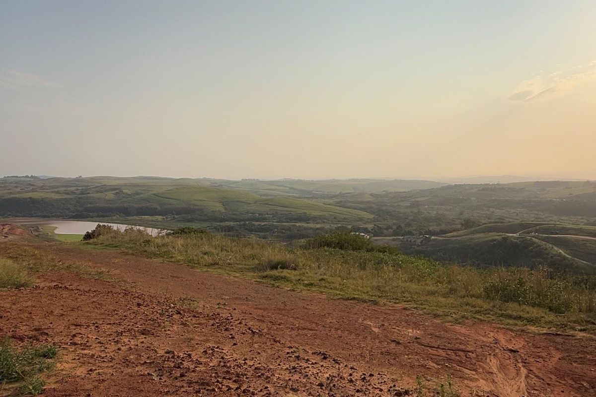 A scenic view overlooking rolling hills and a distant water body from an elevated, undeveloped residential land plot.