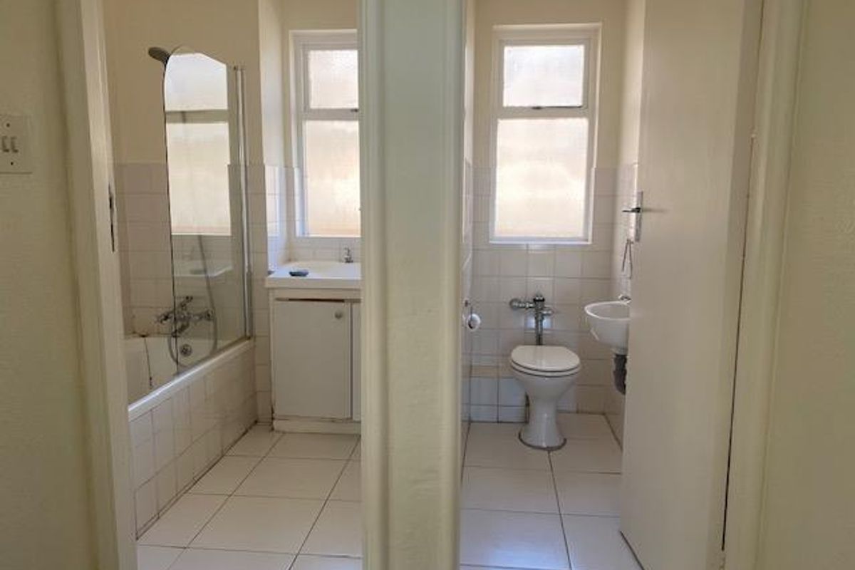 A split-layout bathroom featuring a separate bathtub with shower screen on one side and a toilet with a small basin on the other.