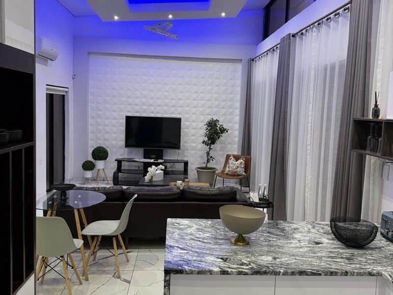 Modern open-plan living and kitchen area featuring high-gloss cabinetry, stone countertops, marble-look flooring, and sophisticated recessed ceiling lighting with blue accent features.