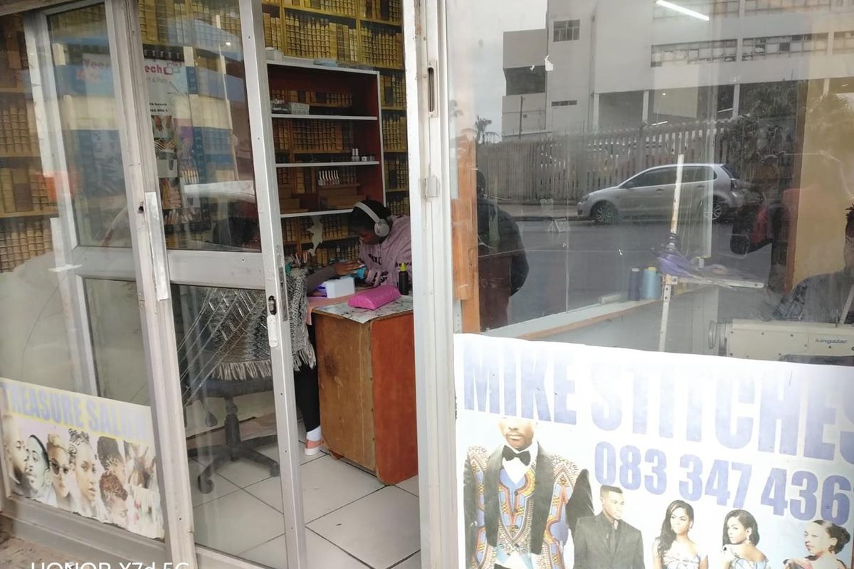 Small retail shop entrance featuring glass storefront doors, tiled flooring, and built-in shelving units suitable for a service-based business.