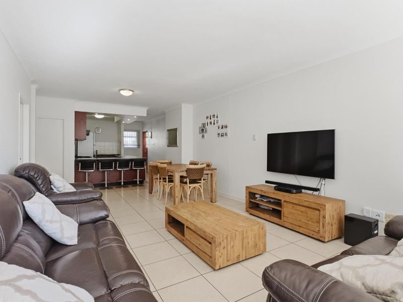 Open-plan living and dining area featuring tiled flooring and a connected kitchen with a breakfast bar, offering a functional and spacious layout.