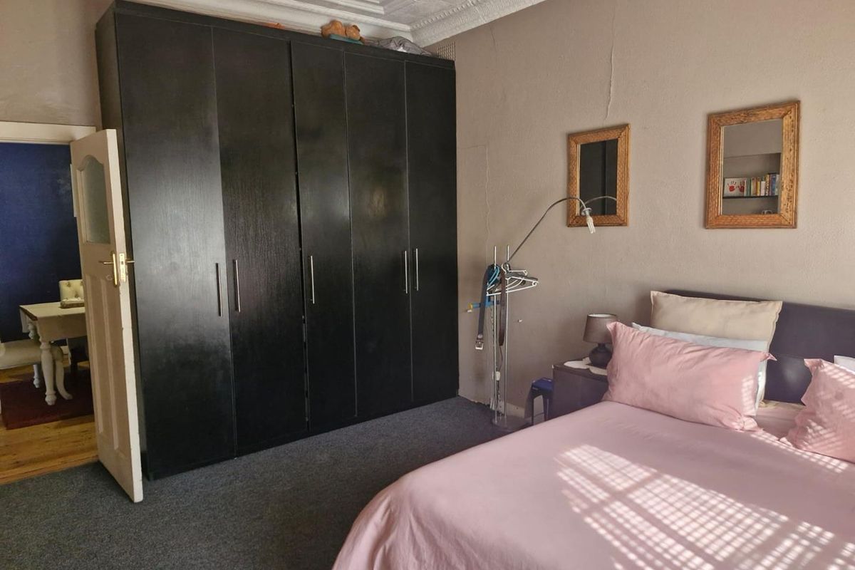 A bedroom featuring a large built-in wardrobe, ornate ceiling detailing, and carpet flooring, showing some signs of wear on the wall plaster.