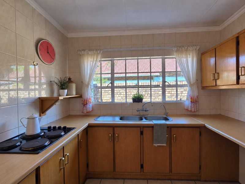 A functional kitchen featuring wooden cabinetry, laminate countertops, a double bowl stainless steel sink, and a built-in electric hob with tiled splashback.