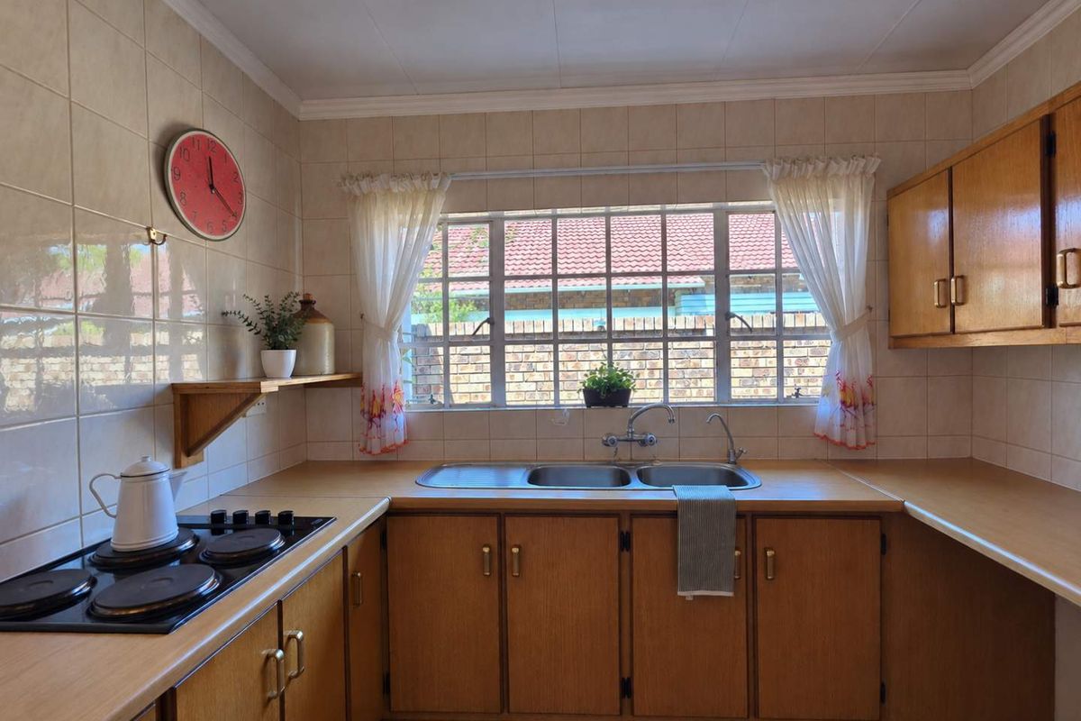 A functional kitchen featuring wooden cabinetry, laminate countertops, a double bowl stainless steel sink, and a built-in electric hob with tiled splashback.
