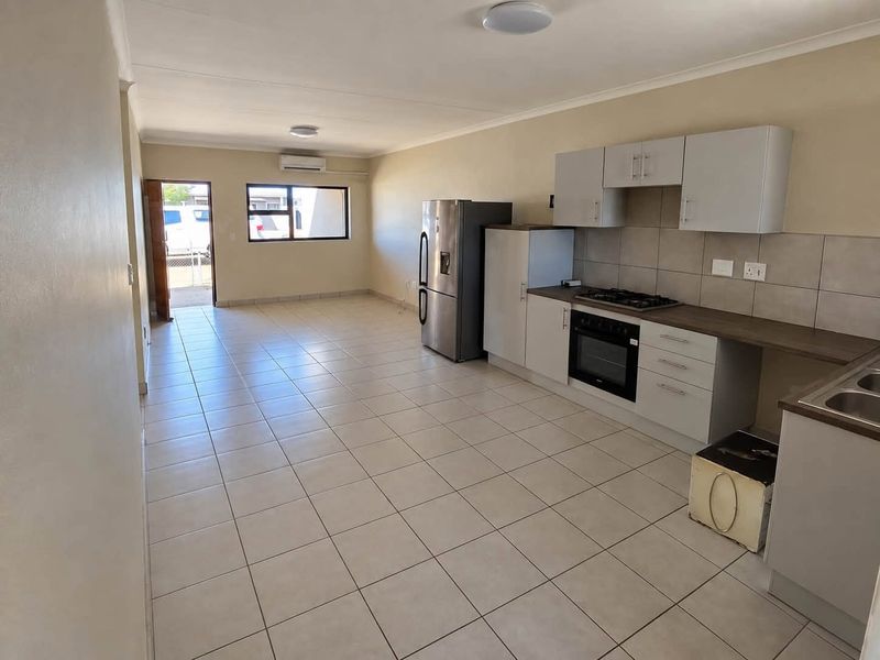 Spacious open-plan living area featuring a modern kitchen with built-in cabinetry, gas hob, electric oven, and neutral tiled flooring throughout.