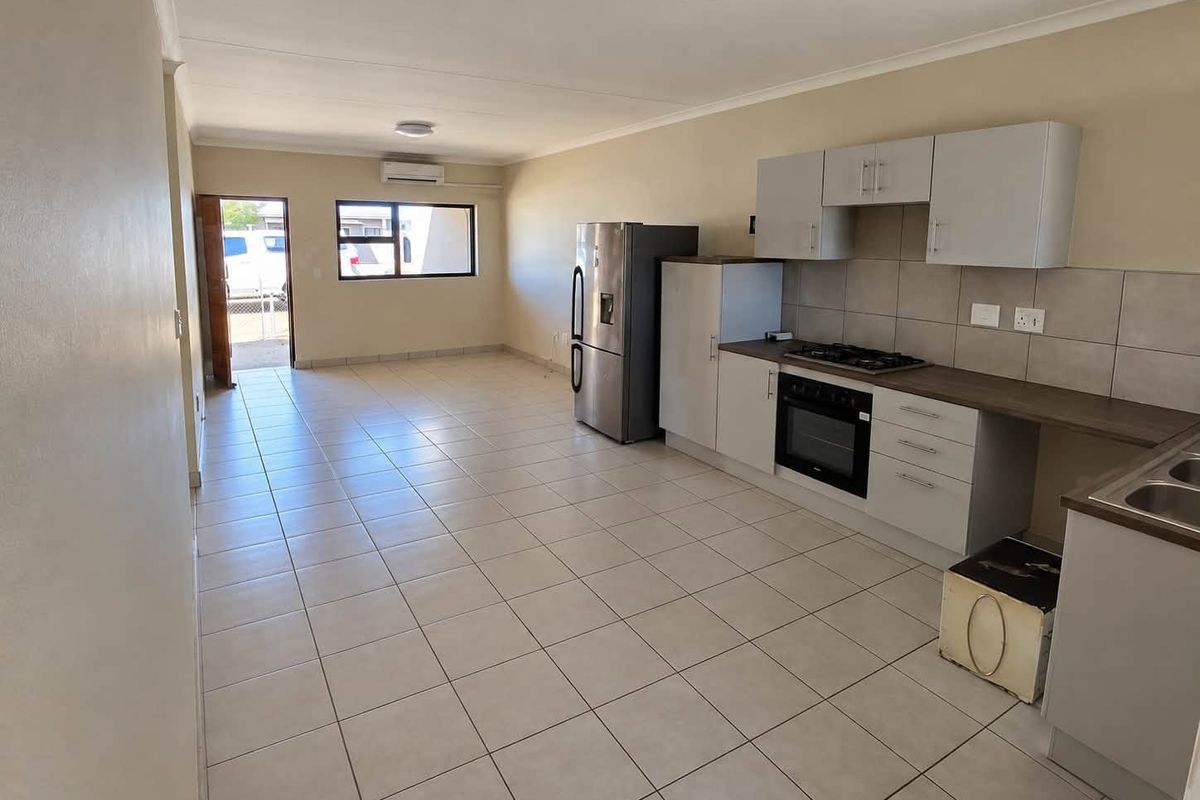 Spacious open-plan living area featuring a modern kitchen with built-in cabinetry, gas hob, electric oven, and neutral tiled flooring throughout.