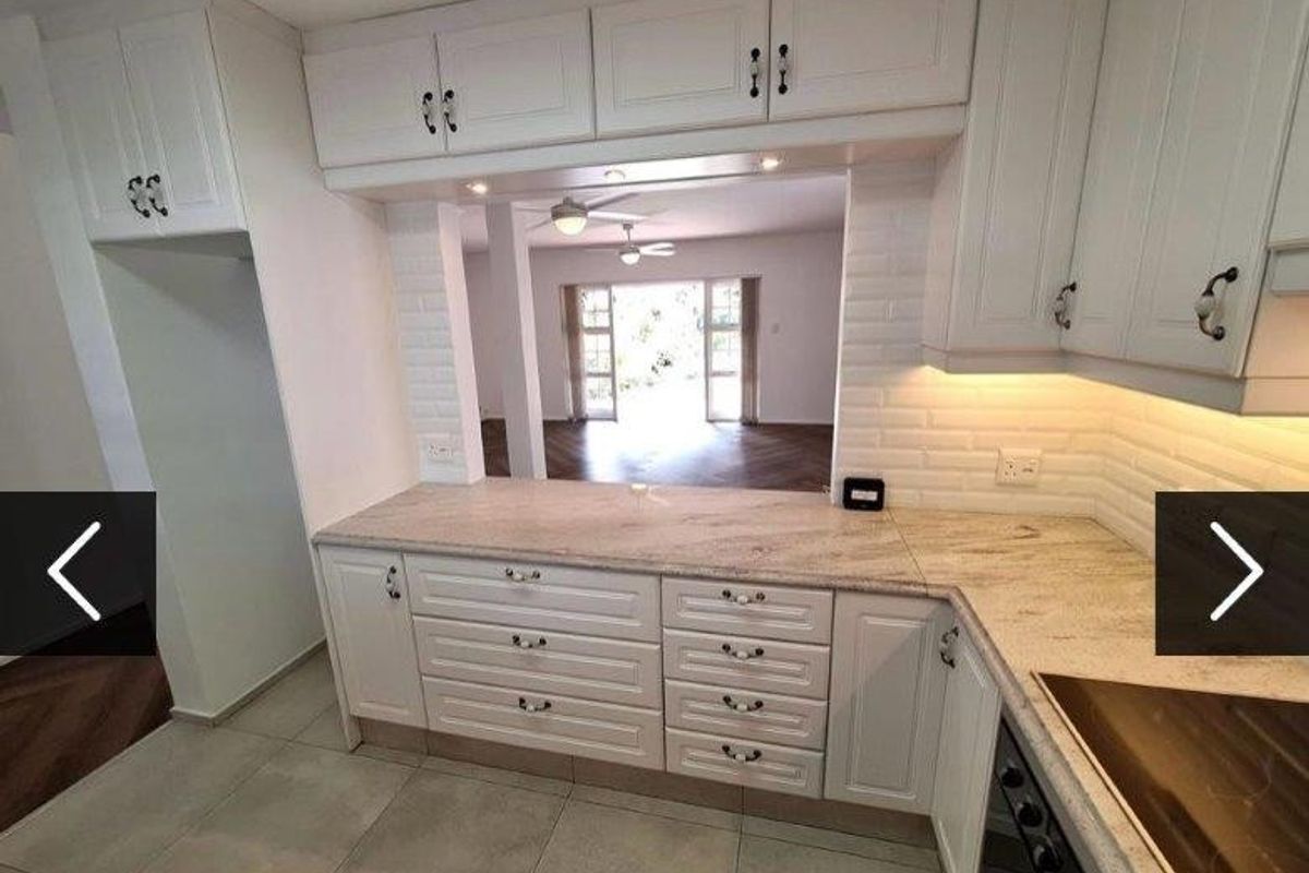 A well-maintained kitchen featuring white cabinetry, stone countertops, and a subway tile backsplash, with a convenient pass-through window overlooking the living area.