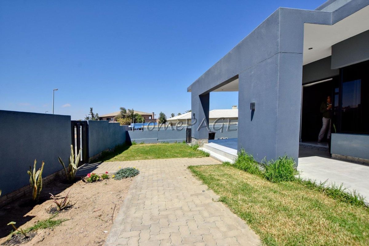 Rear exterior view featuring a paved walkway, lawn area, and a covered patio attached to the main building structure.