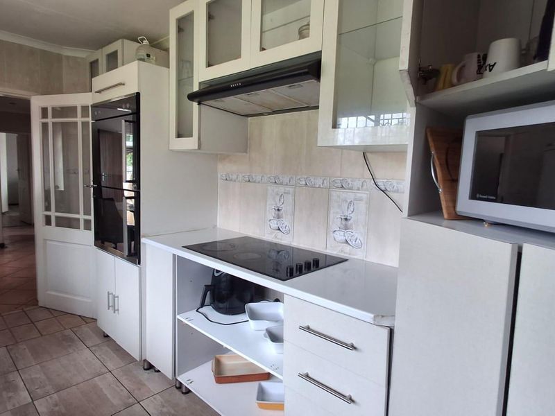 A functional kitchen featuring white cabinetry, a built-in oven, electric hob, extractor fan, and tiled flooring with a neutral backsplash.