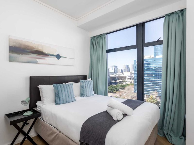 A bright bedroom featuring large floor-to-ceiling windows that offer expansive city views and provide ample natural light.