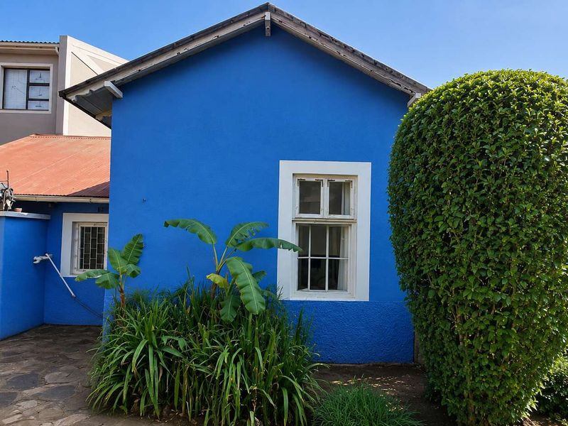Rear view of the property featuring a vibrant blue facade, solar geyser, metal roofing, and stone paved courtyard area.