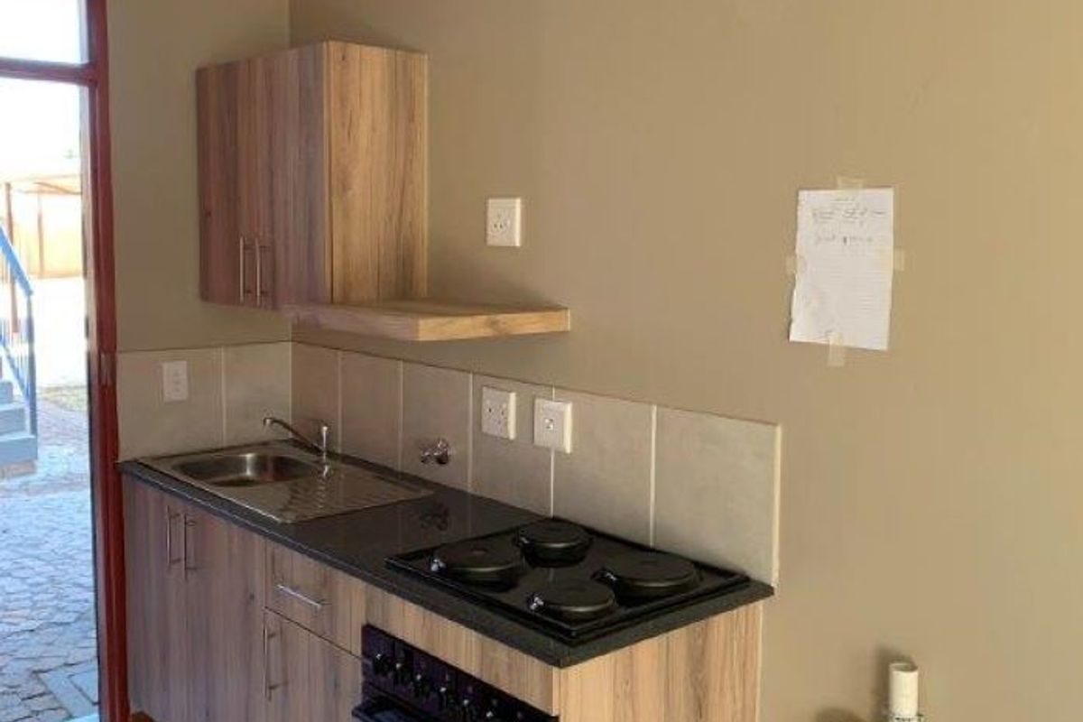 A compact kitchen featuring wood-look cabinetry, a built-in oven with electric hob, stainless steel sink, and tiled backsplash, with direct access to the exterior.