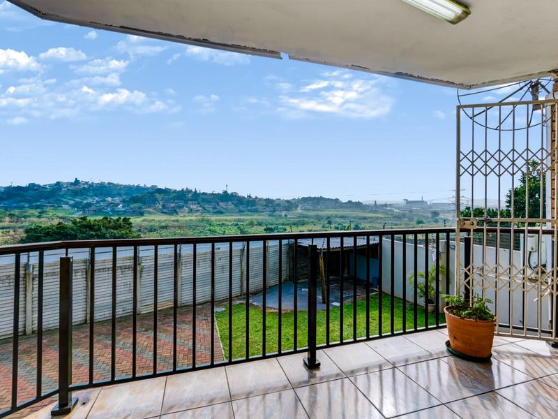 A covered balcony featuring tiled flooring, a metal balustrade, and a security gate, offering expansive views over the surrounding landscape and garden area.