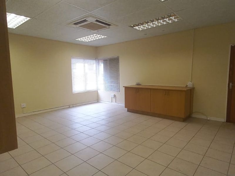 An empty office space featuring tiled flooring, a suspended ceiling with recessed lighting, integrated air conditioning, and built-in storage cabinetry.