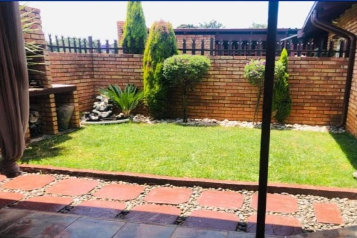 A private rear garden featuring a brick boundary wall, paved walkway, manicured lawn, and a built-in brick braai area.